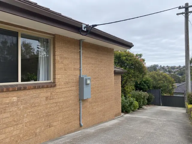 Overhead service cable and bracket on a brick house exterior with meter box and driveway in Beacon Hill
