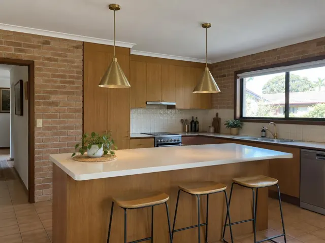 Two brass pendant lights above a kitchen island in a brick-walled home with wood cabinets in Dee Why